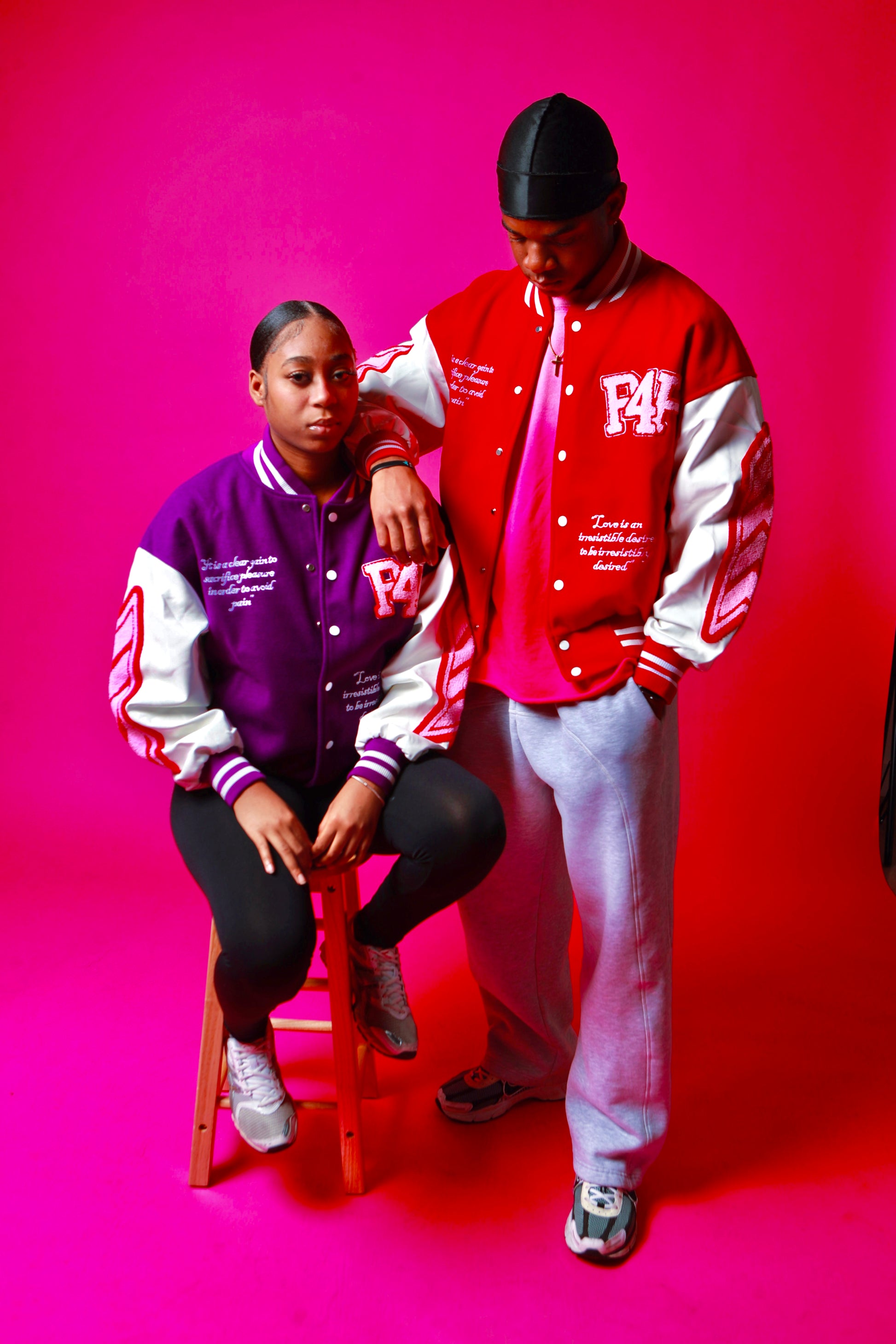 Two people wearing colorful P4P letterman jackets against a pink background